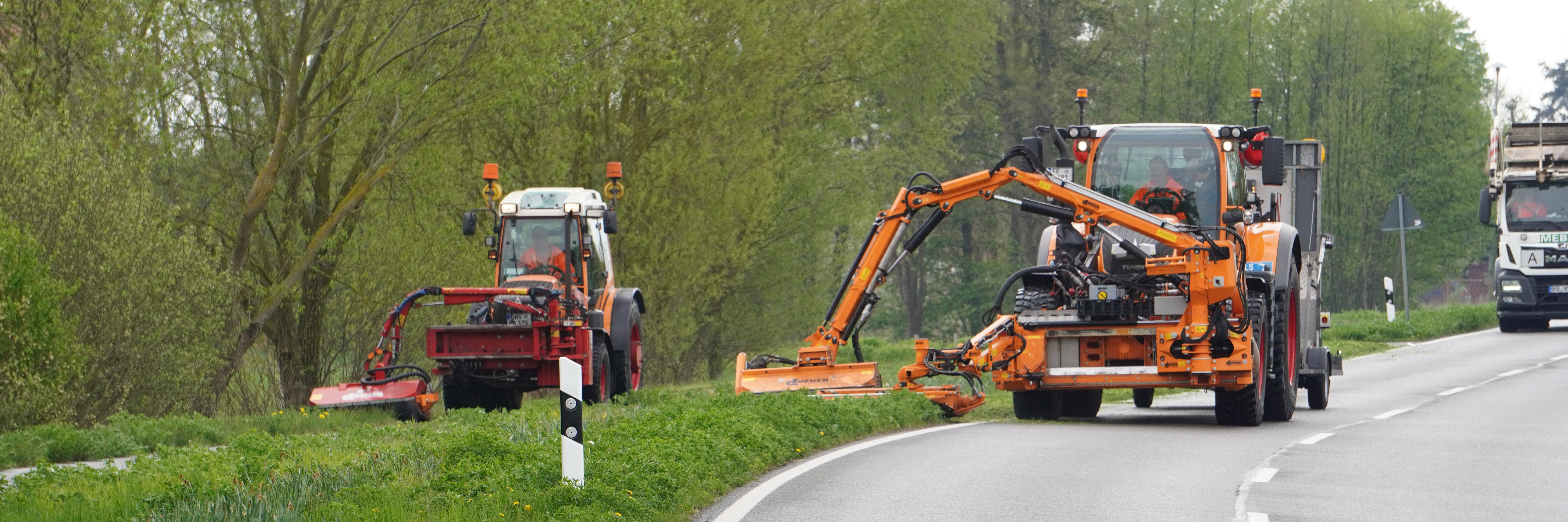 Ein Unimog mäht den Randstreifen, zwischen Fahrbahn und danebenliegendem Radweg befindet sich eine Grünfläche, der Randstreifen des Radweges wird mittels eines Traktos gemäht