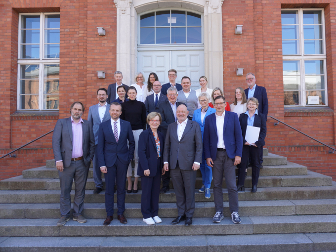 Gruppenfoto der Teilnehmenden vor einem roten Gebäude auf einer Treppe über mehrere Stufen versteilt in der Höhe stehend